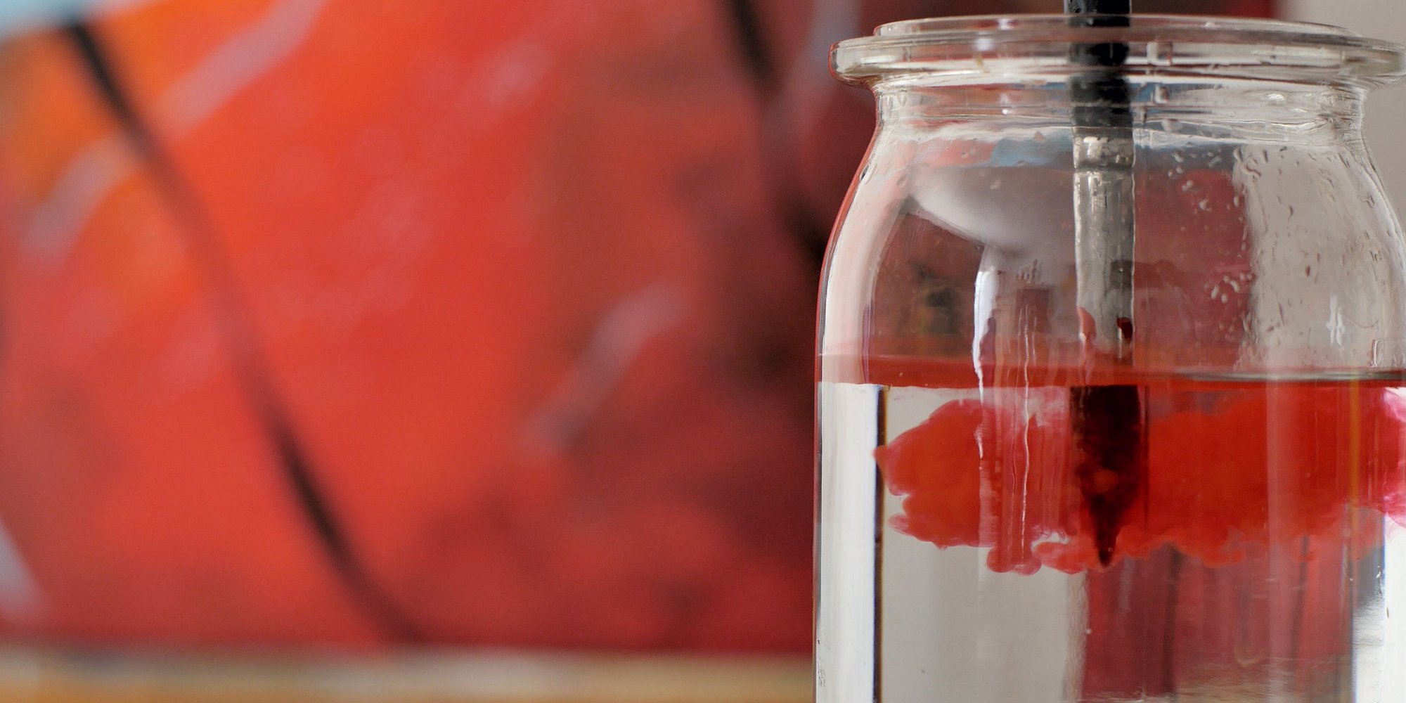 En pensel med rödfärg på doppad i glasburk