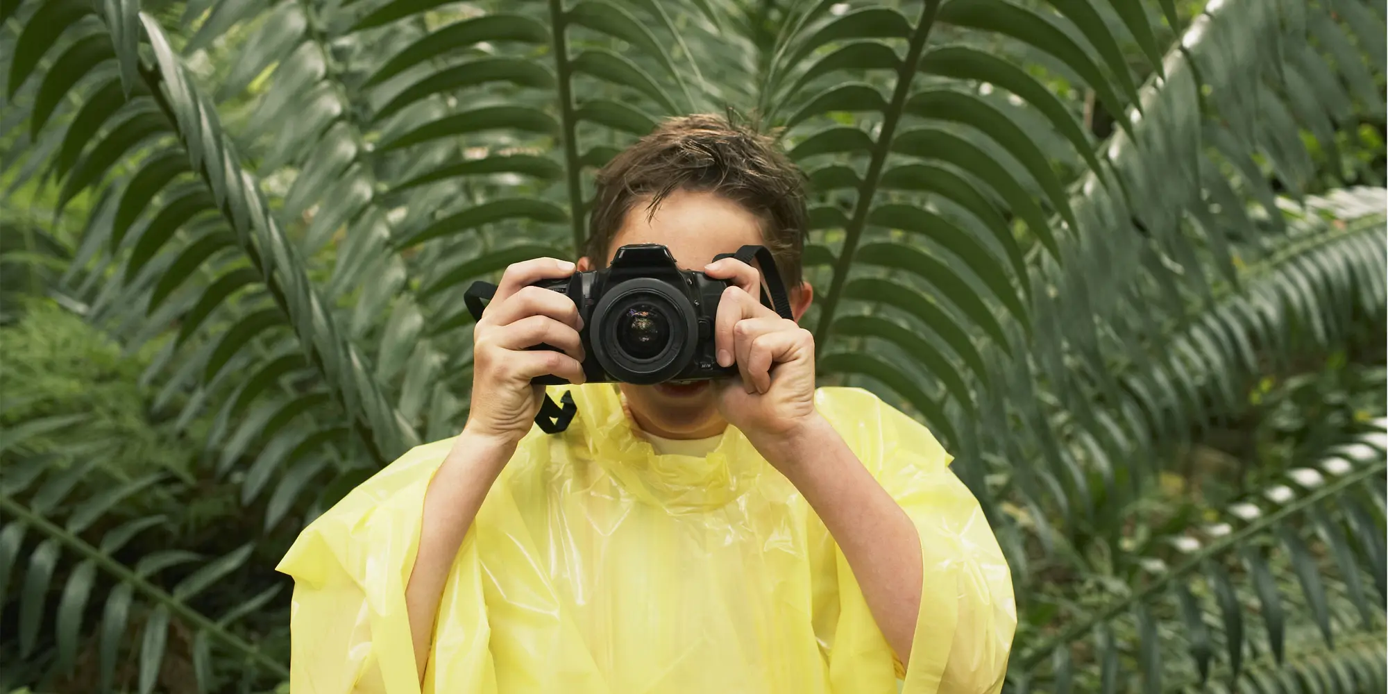 En kille i regnjacka tar bilder i skog