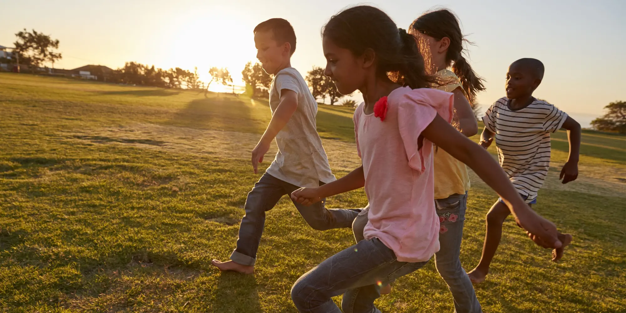 Fyra barn springer barfota på äng i solnedgång