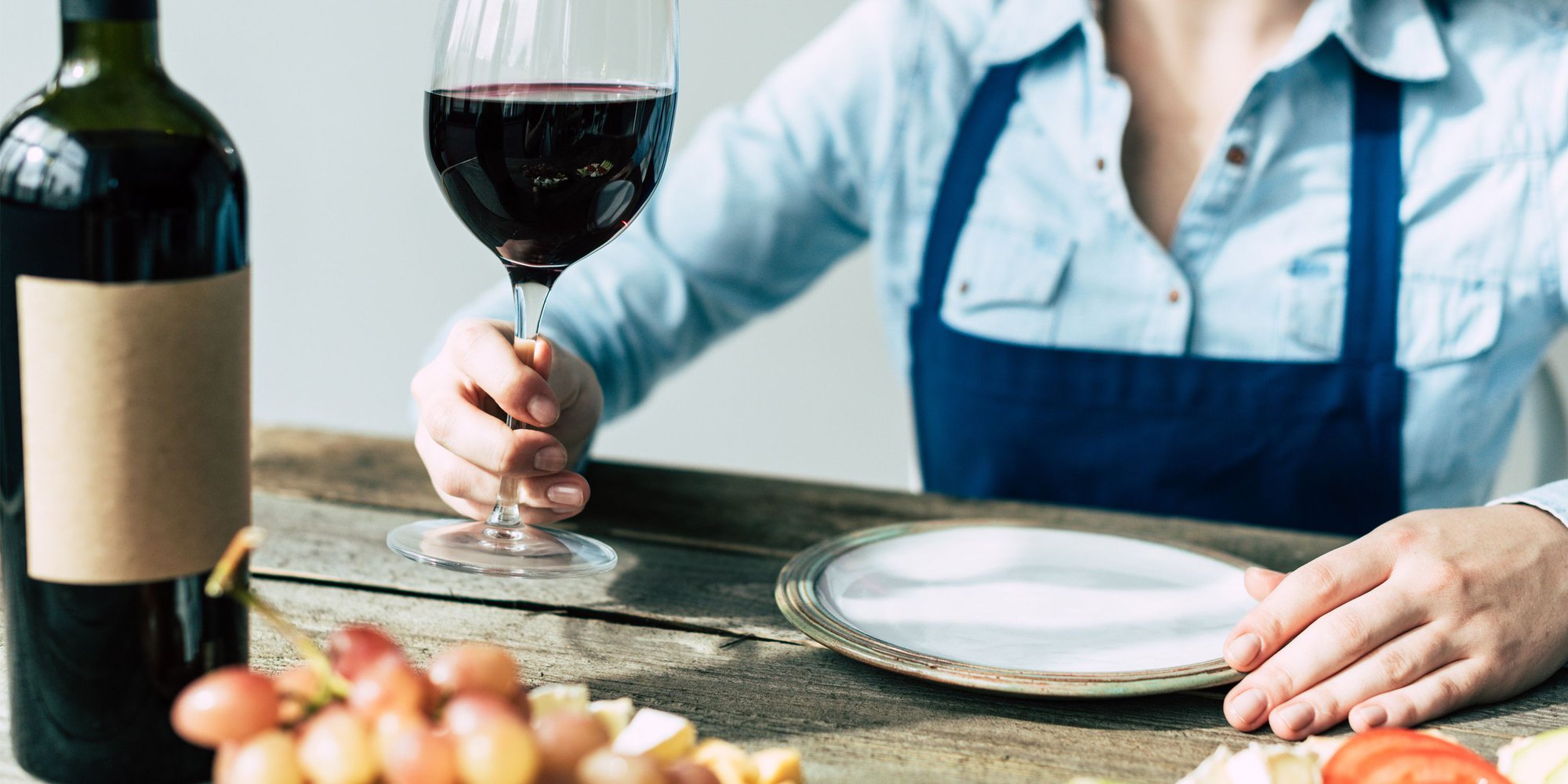 En person sitter vid ett bord och håller i ett glas med rött vin