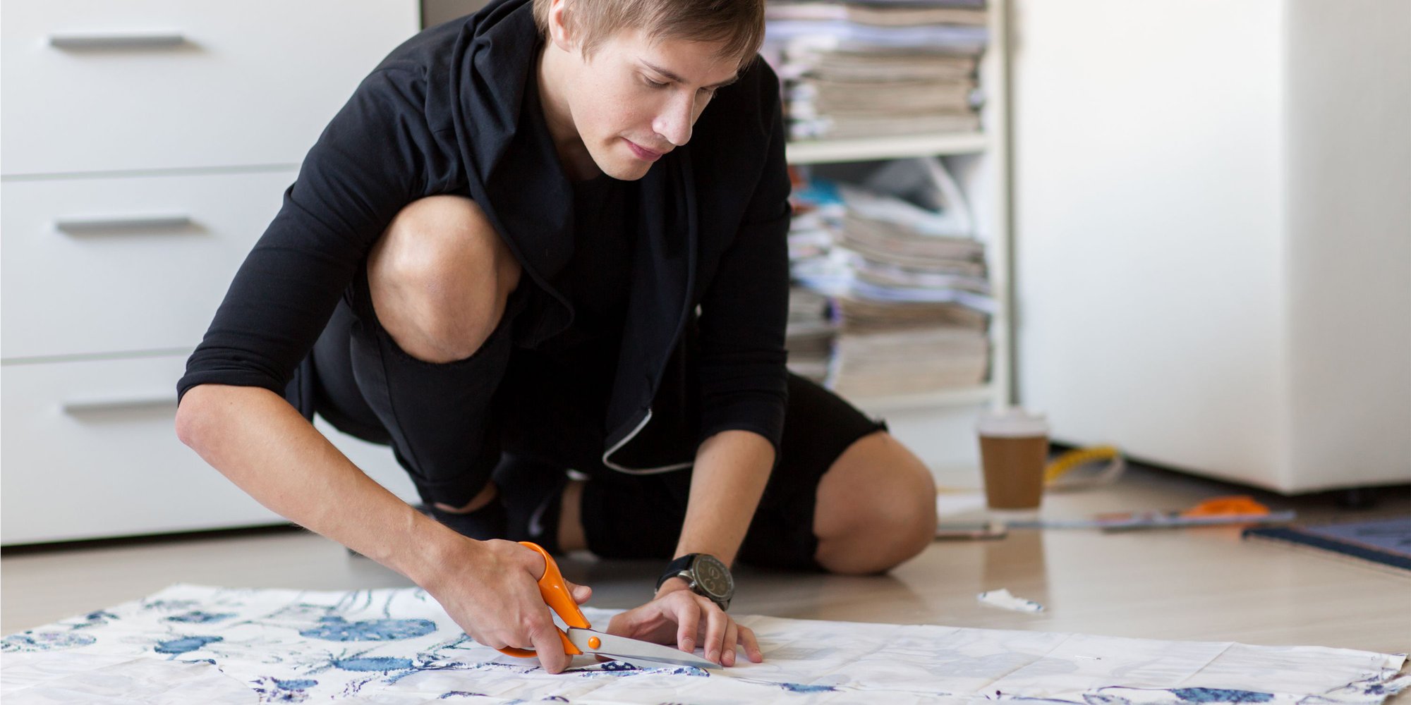 En ung designer sitter på golvet och klipper i ett tyg