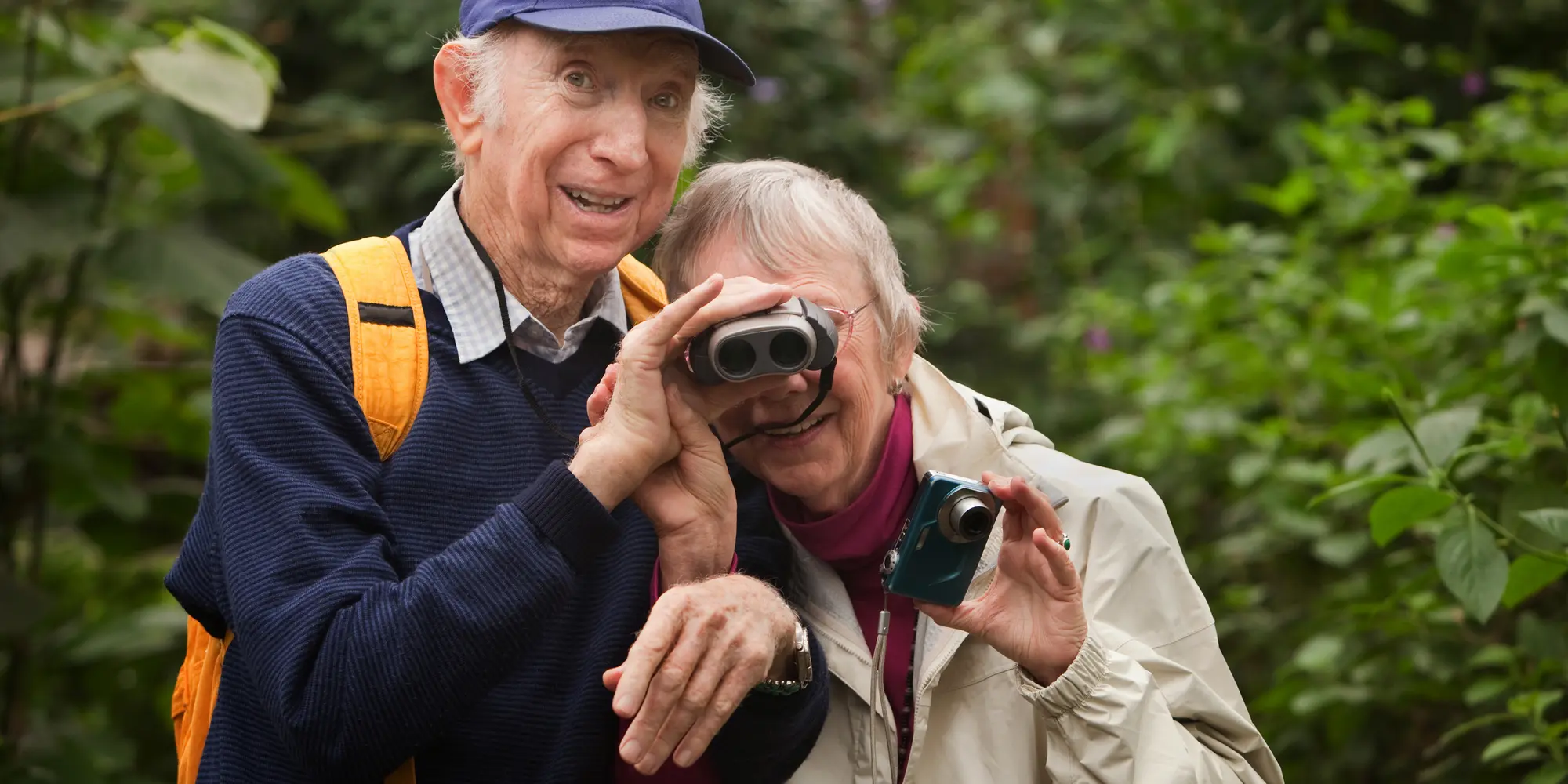 Ett äldre par i naturen med en kikare och en kamera.