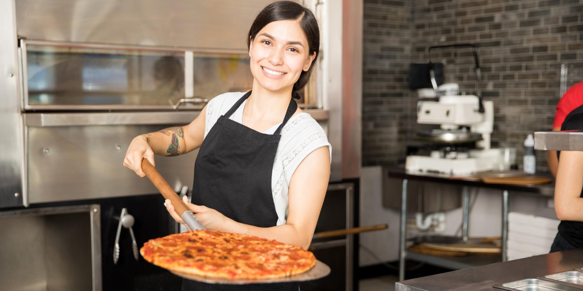 Kvinna som tar ut pizza från pizzaugn