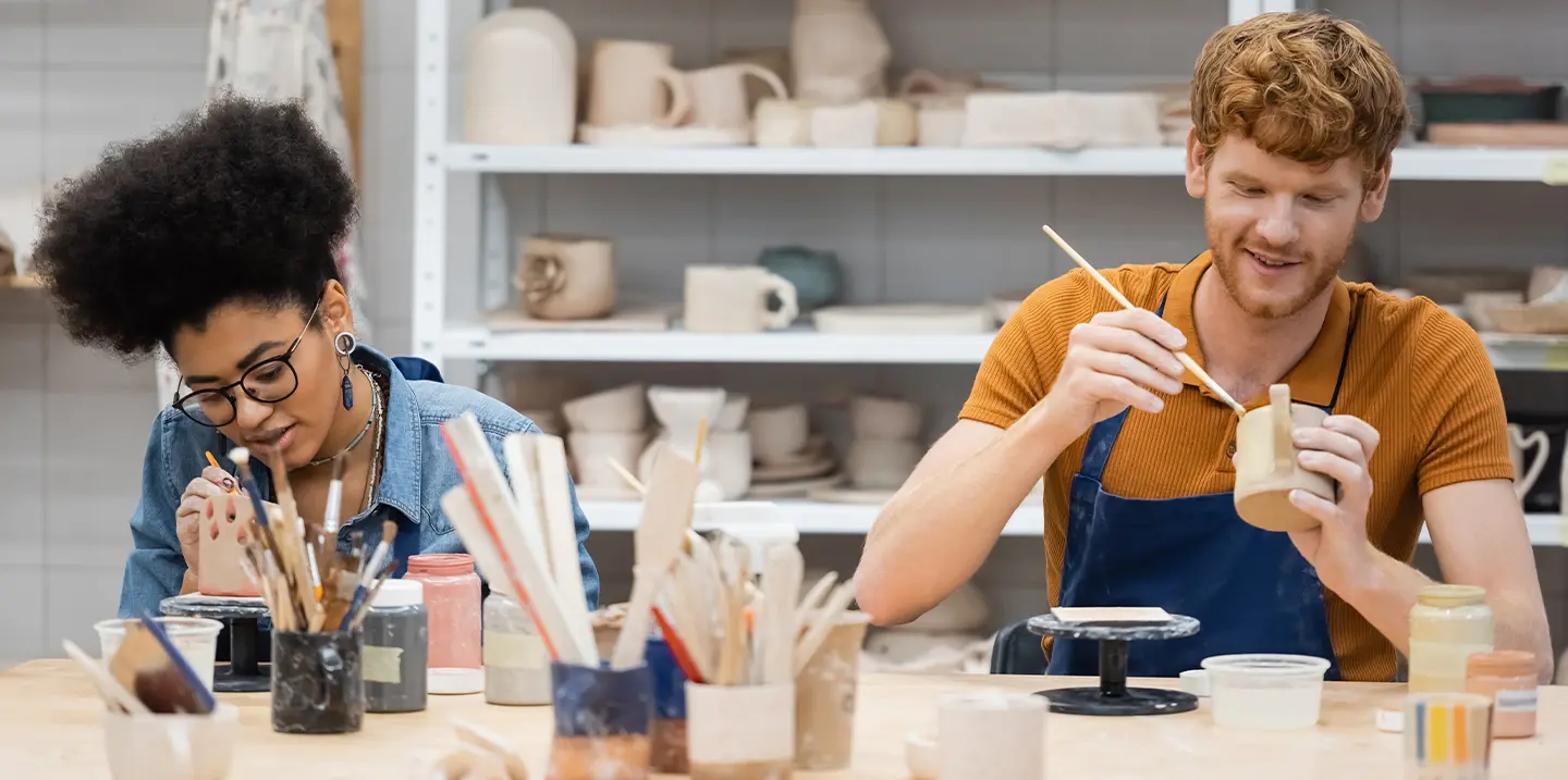 En man och en kvinna målar keramikkoppar i en studio