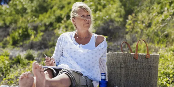 Kvinna som sitter vid en strand och målar  med akvarell