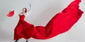En kvinna klädd i en röd och vit flamencodräkt dansar med en röd solfjäder i handen