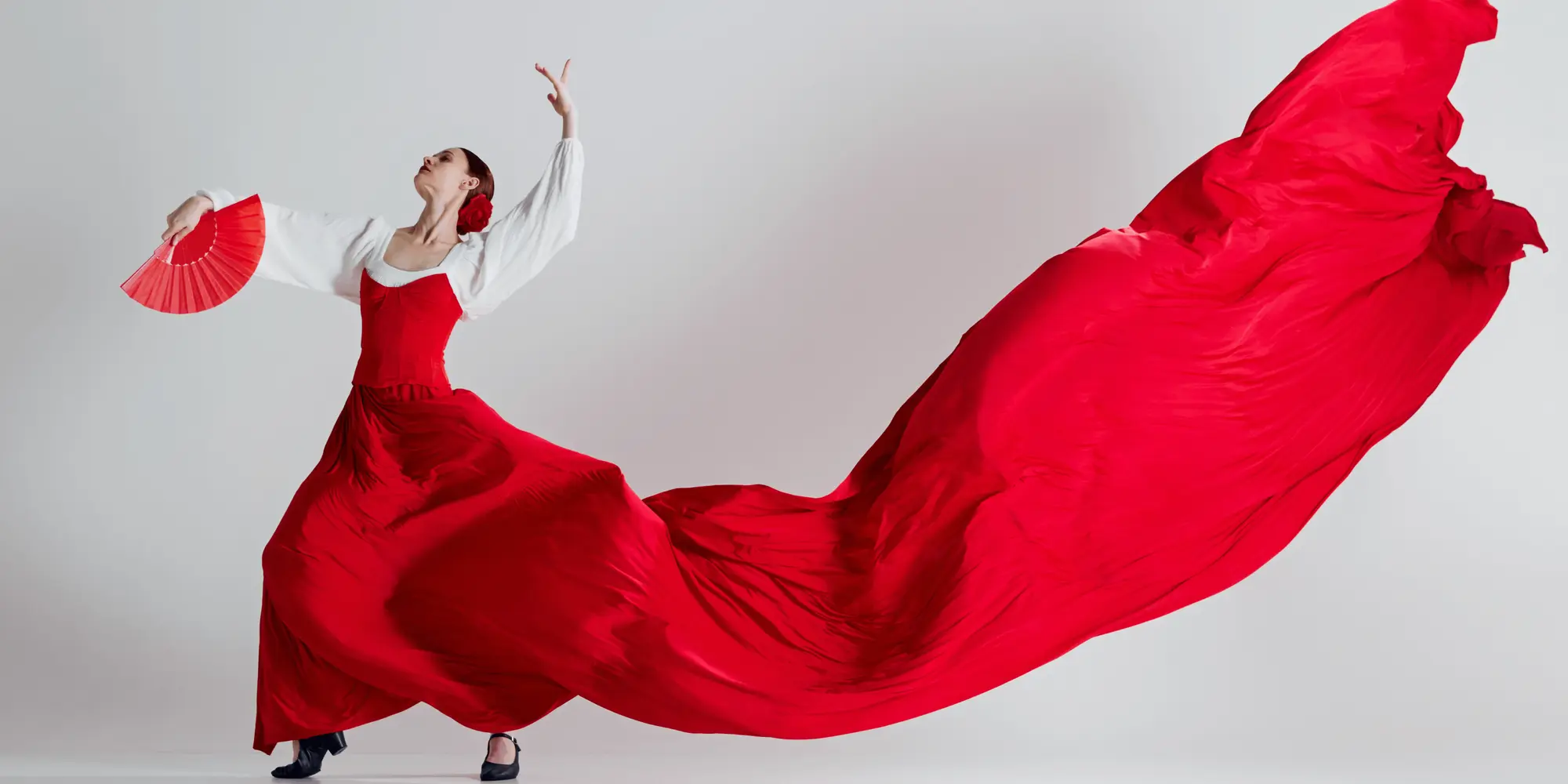 En kvinna klädd i en röd och vit flamencodräkt dansar med en röd solfjäder i handen