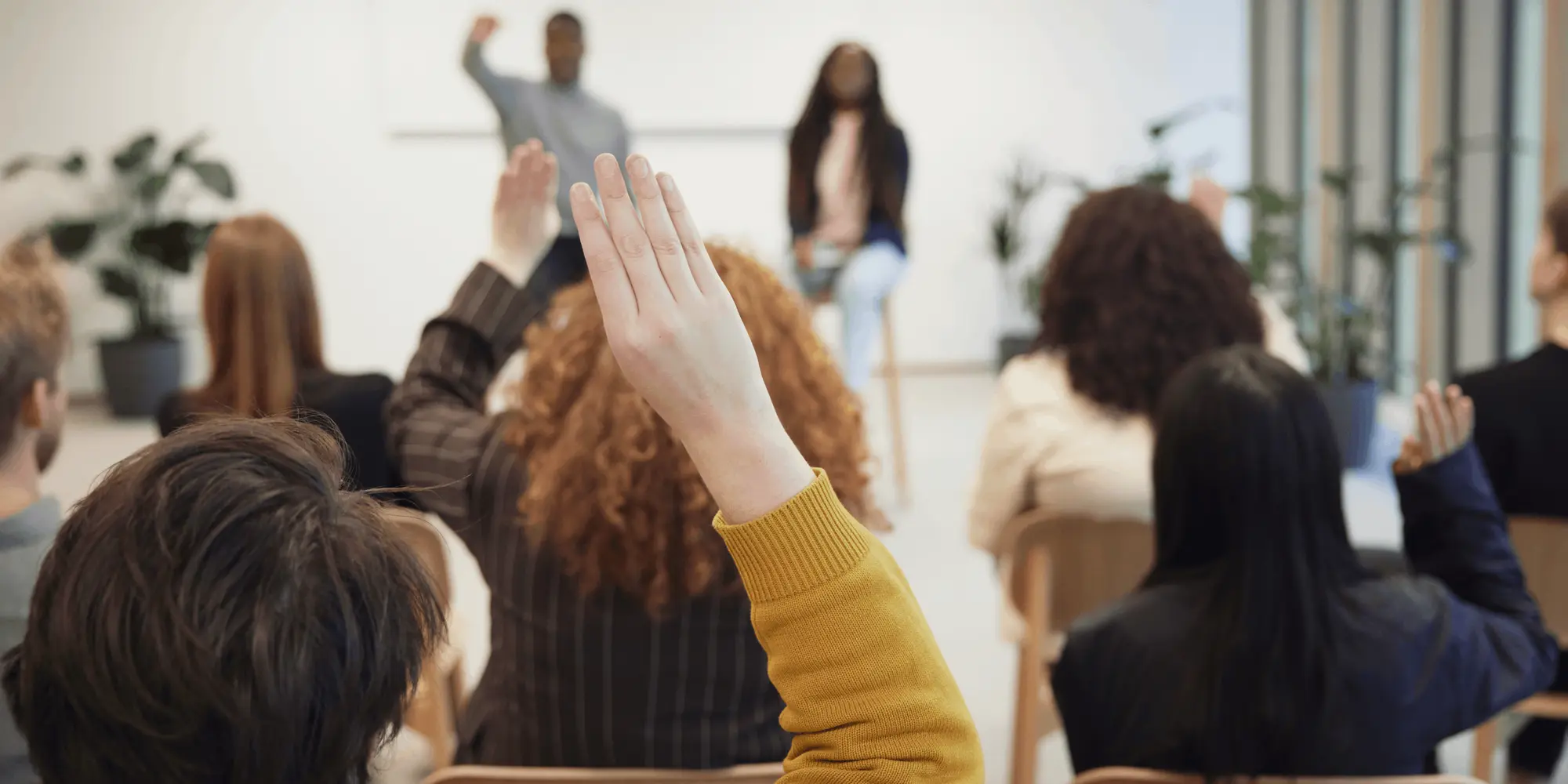 : Personer sitter i ett klassrum eller föreläsningssal med händerna uppsträckta.