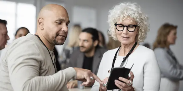 Två kursdeltagare samtalar och tittar på en mobiltelefon under en paus i en utbildning eller workshop.