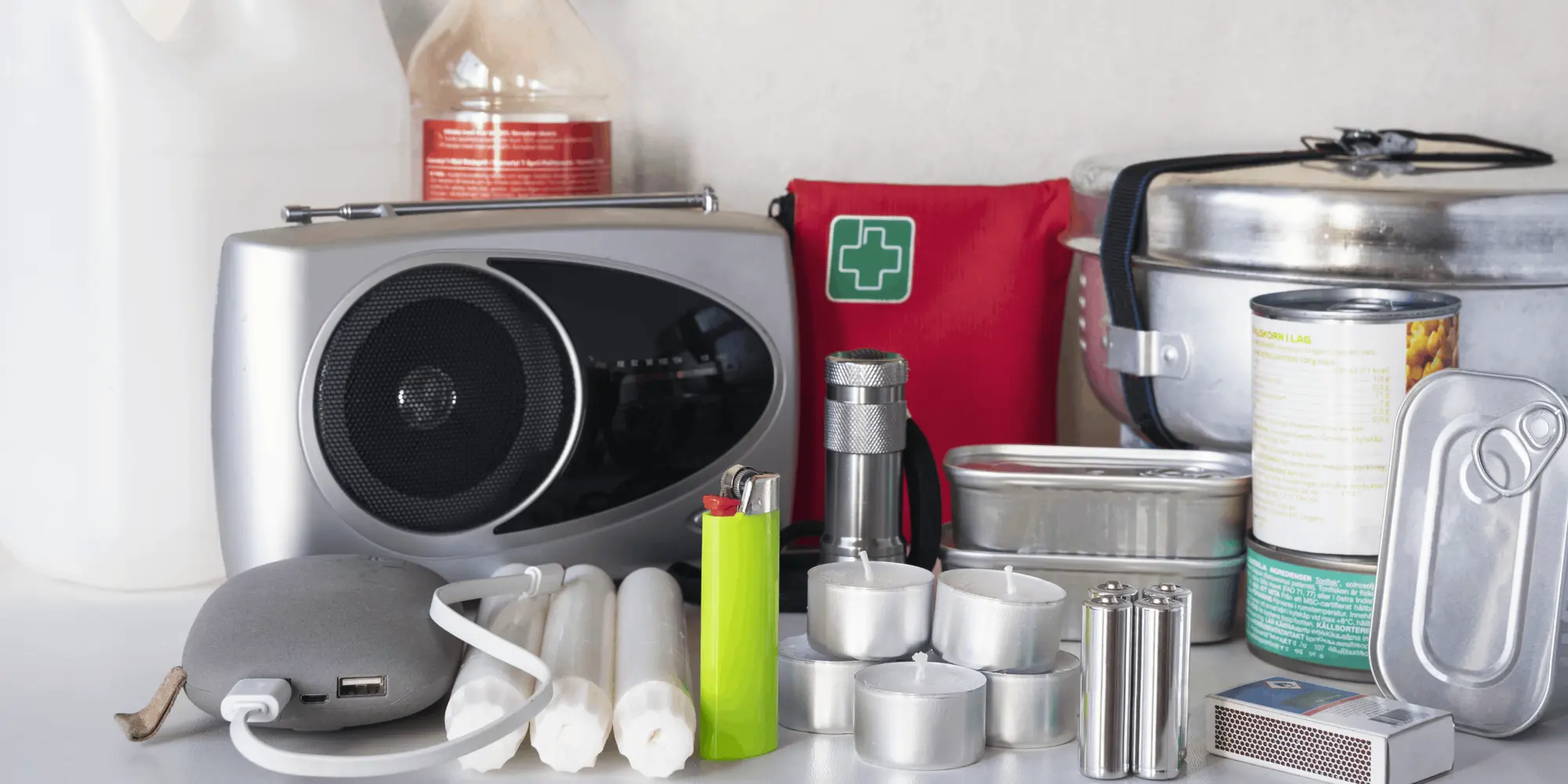 Nödutrustning på ett bord, inklusive radio, ficklampa, ljus, konserver, vattenflaskor, första hjälpen-kit och powerbank