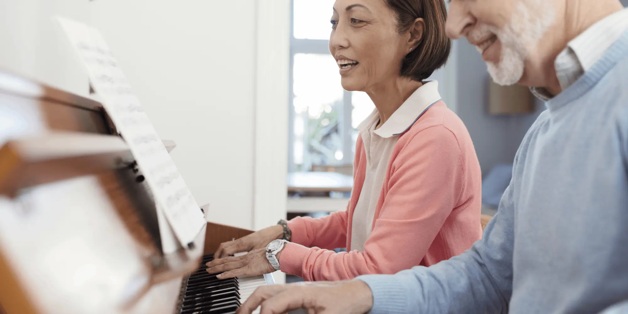 Två vuxna personer spelar piano tillsammans och följer notblad