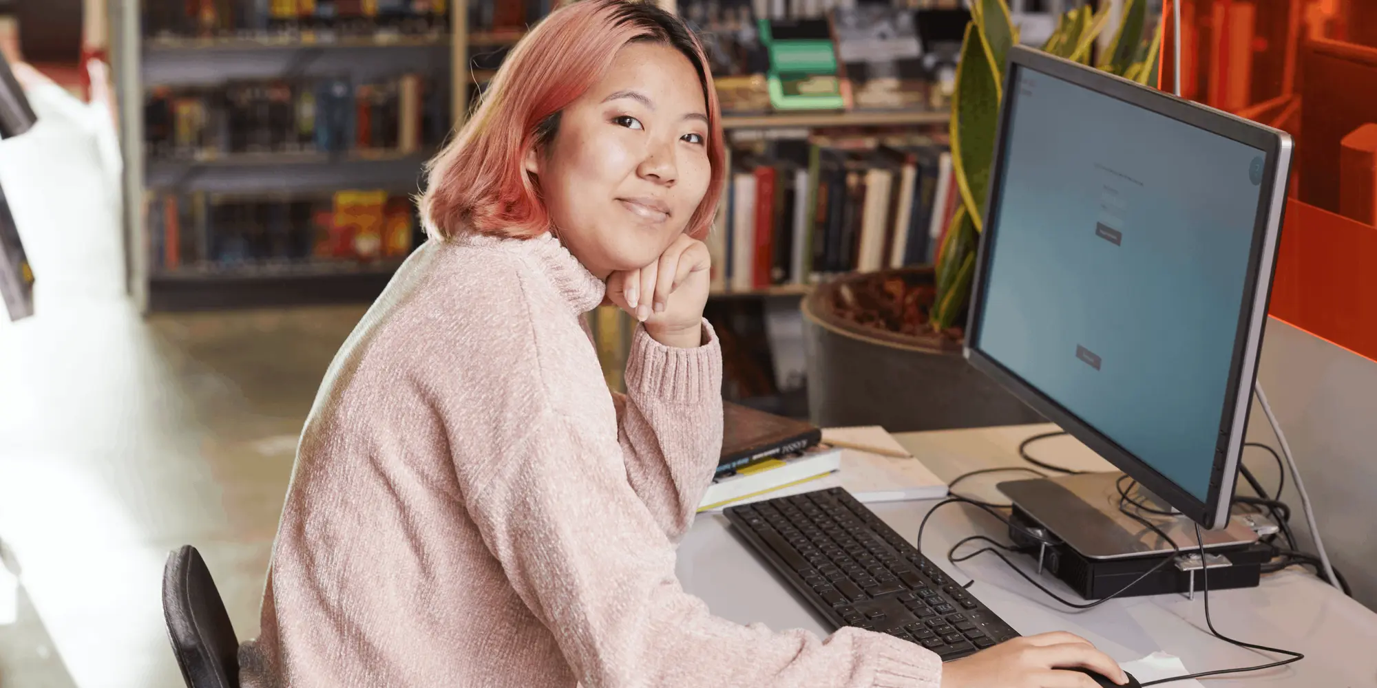 Ung kvinna arbetar vid dator i biblioteksmiljö – deltar i kurs i kodning och programmering för nybörjare.