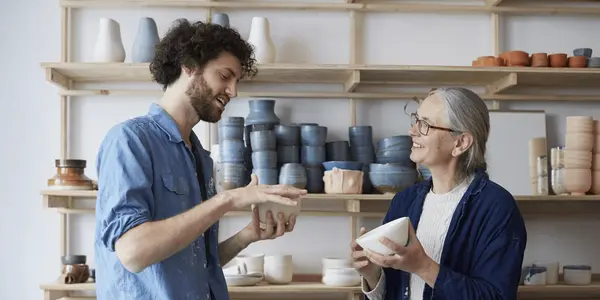 Två personer samtalar och håller i keramikskålar i en verkstad