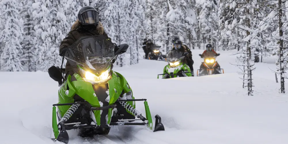 Personer kör snöskoter genom ett snötäckt vinterlandskap bland snötäckta träd