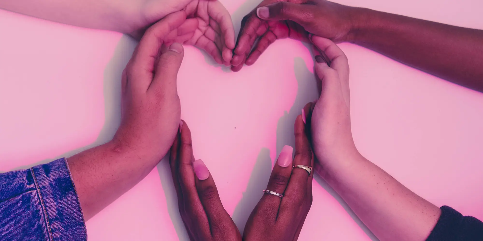 Händer bildar ett hjärta med rosa bakgrund.