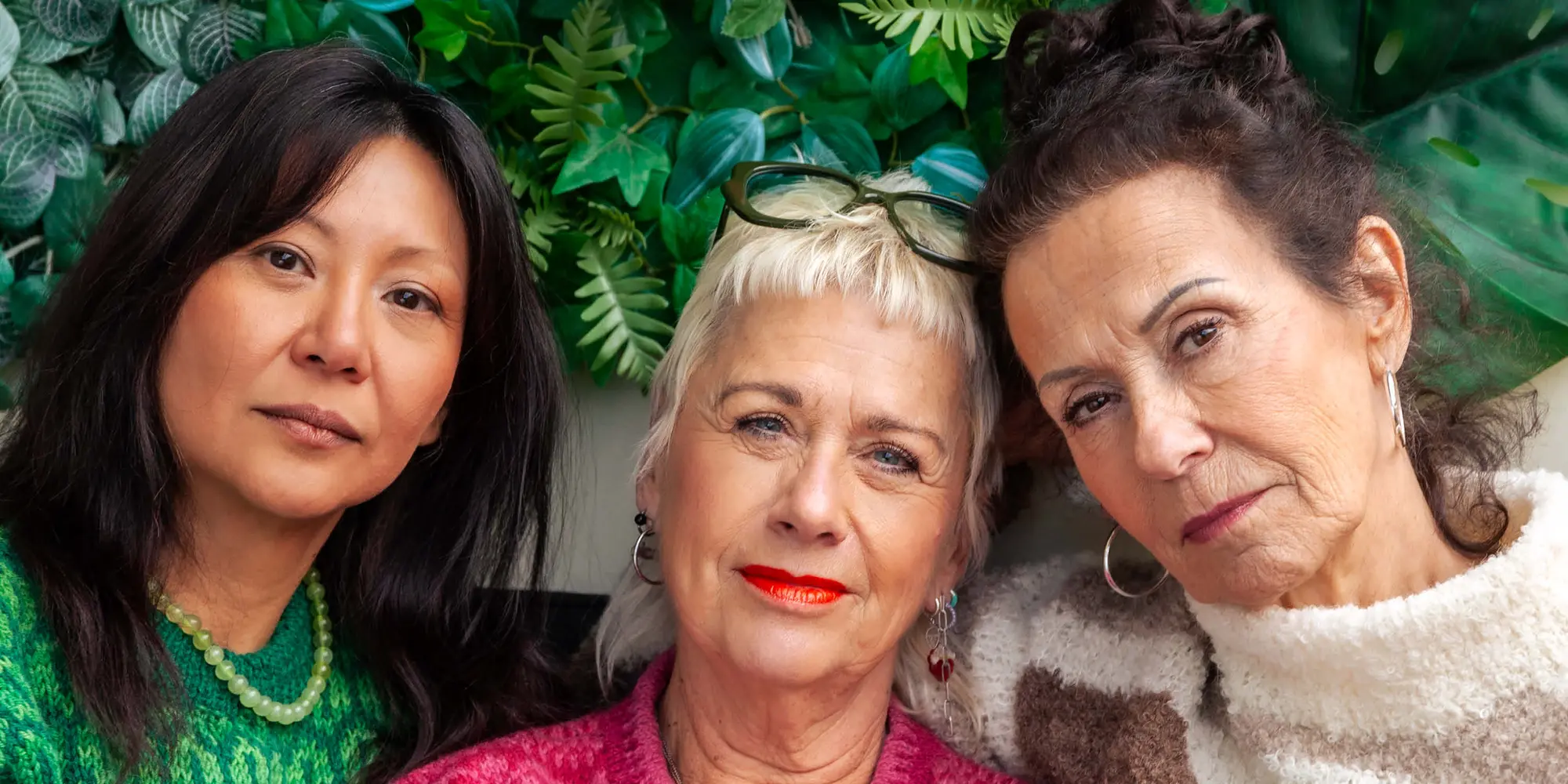 Tre kvinnor ser in i kameran med grönska i bakgrunden.