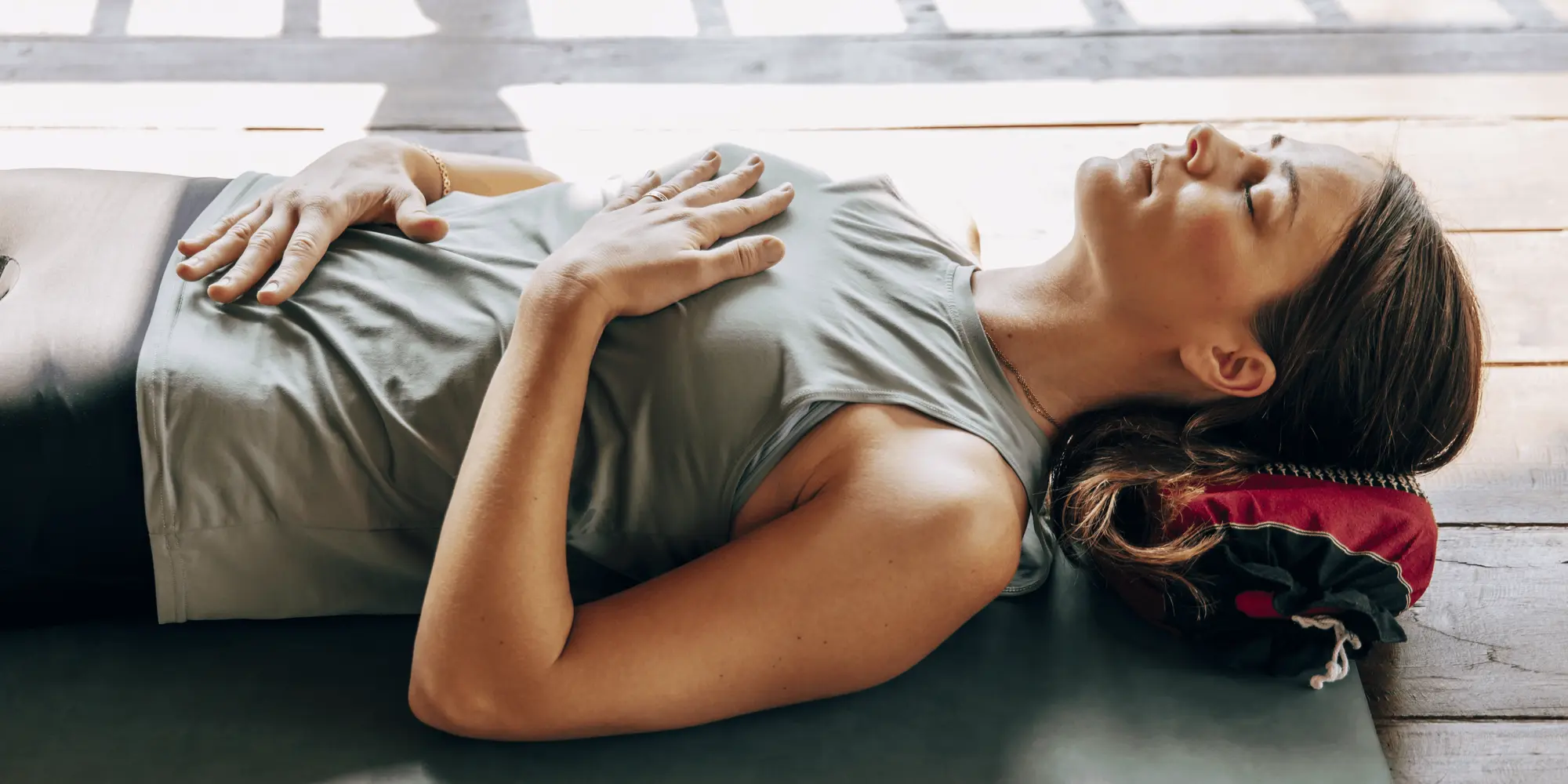 Kvinna ligger på rygg på en yogamatta med ögonen slutna och händerna vilande på mage och bröst.