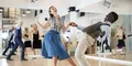 Par dansar energiskt lindy hop eller charleston i en spegelsal. Kvinnan bär blå kjol och rutig blus, mannen beige byxor och väst