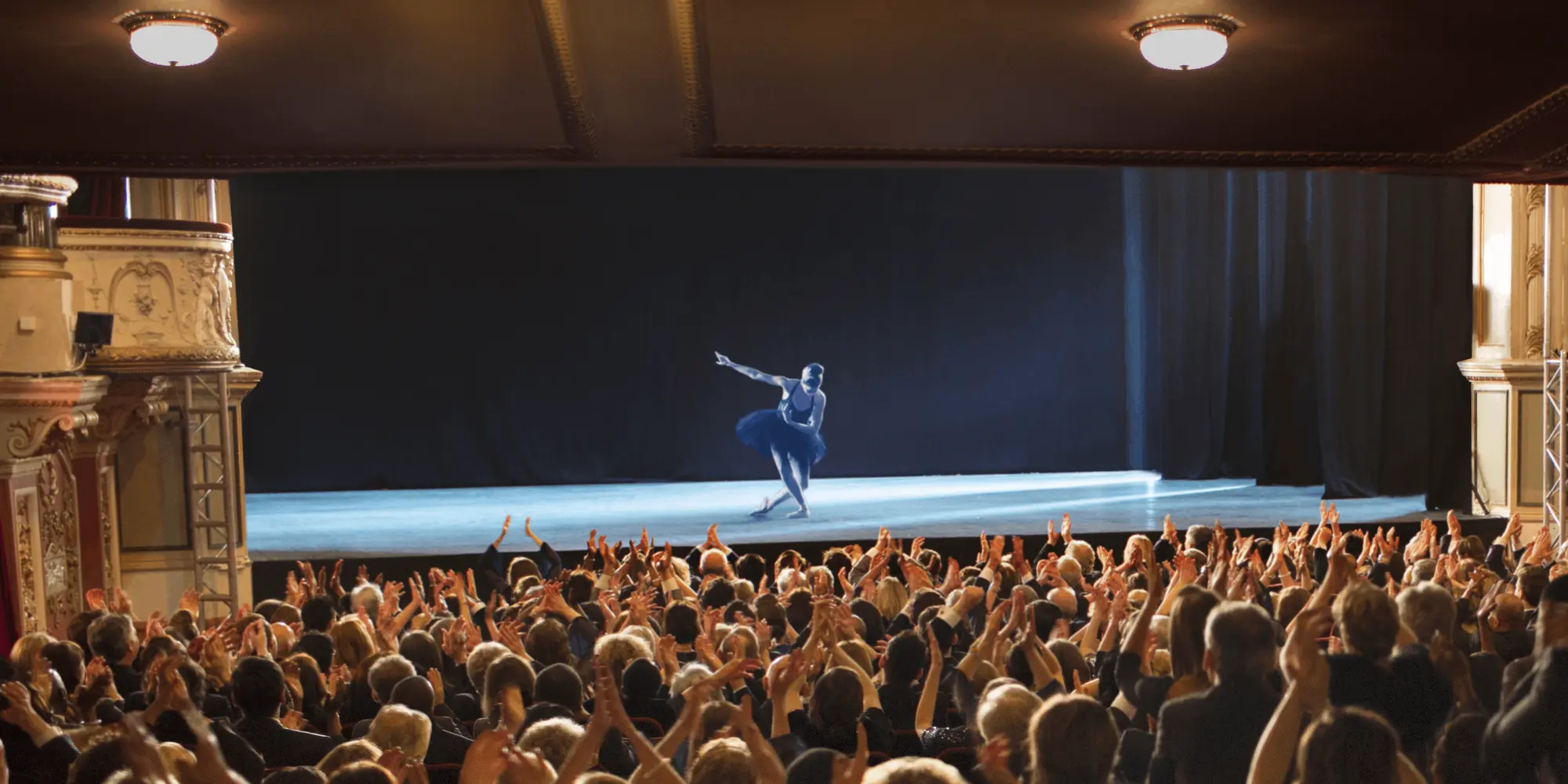 Publik applåderar entusiastiskt i en elegant teatersalong medan en dansare avslutar sitt nummer ensam på scenen