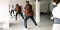 En danslärare i röd hoodie leder en grupp ungdomar i en ljus dansstudio med spegelväggar