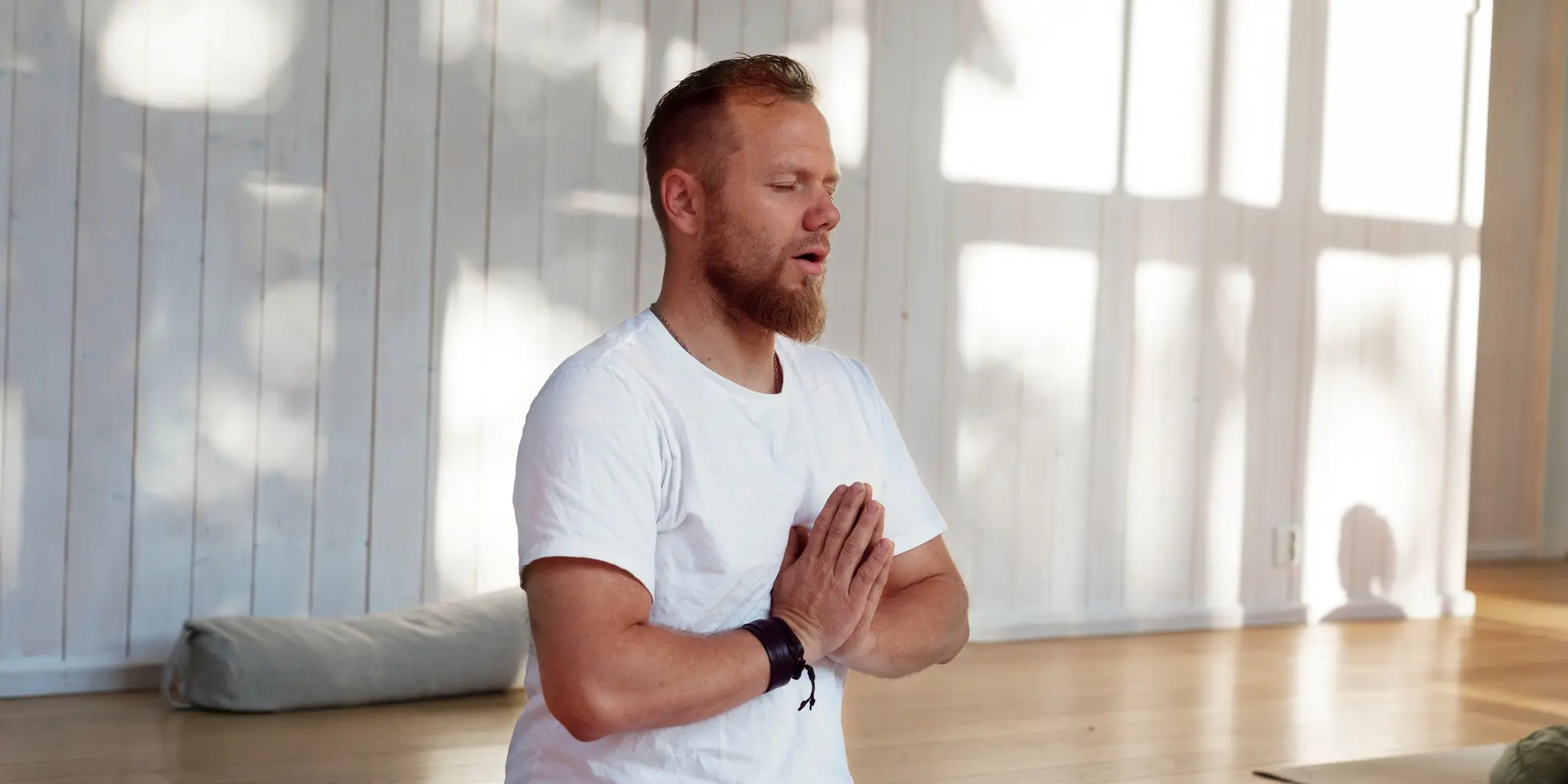 En man i vita kläder sitter på golvet och gör yoga