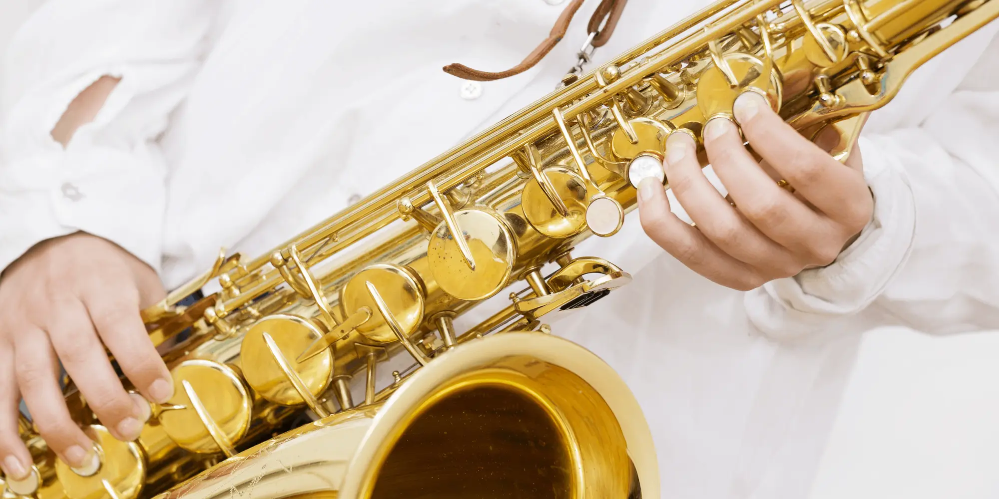 Närbild på en person som spelar saxofon, iklädd vit skjorta