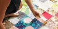 Kvinna sitter på golvet och syr ihop färgglada lappar till ett lapptäcke i ett patchwork-mönster.