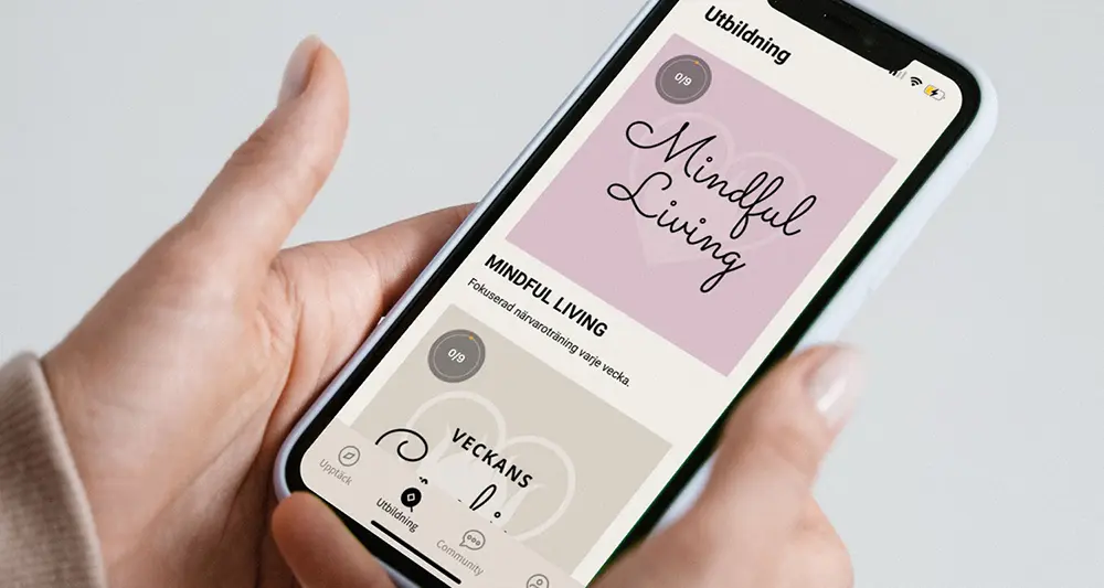 Händer håller en mobiltelefon med appen Lyckans Smed uppe.