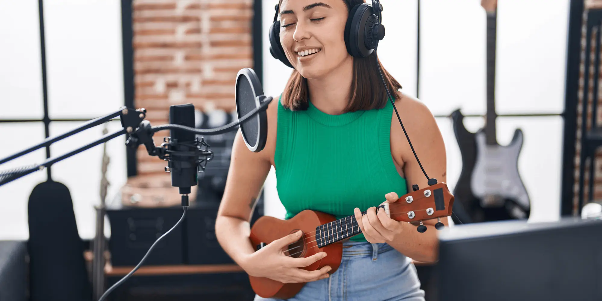 Ung kvinna sjunger och spelar ukulele i en hemmastudio med mikrofon och inspelningsutrustning
