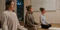 Tre kvinnor sitter i meditationsställning på yogamattor i ett lugnt inomhusrum med trägolv och vita väggar.